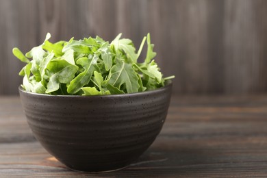 Photo of Fresh ripe green arugula leaves on dark wooden table, closeup. Space for text