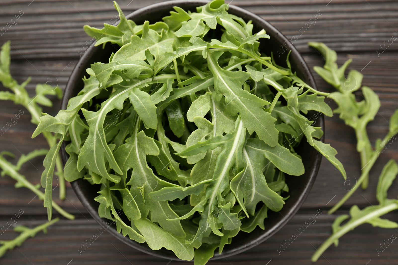 Photo of Fresh ripe green arugula leaves on dark wooden table, flat lay