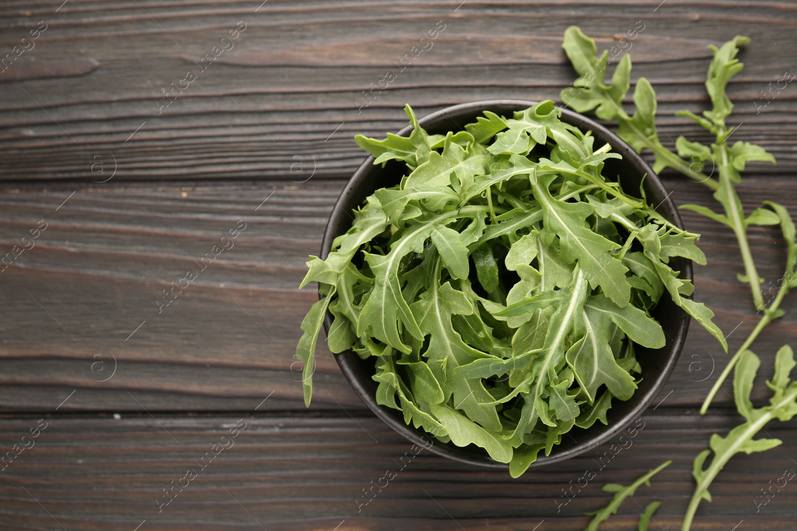 Photo of Fresh ripe green arugula leaves on dark wooden table, top view. Space for text