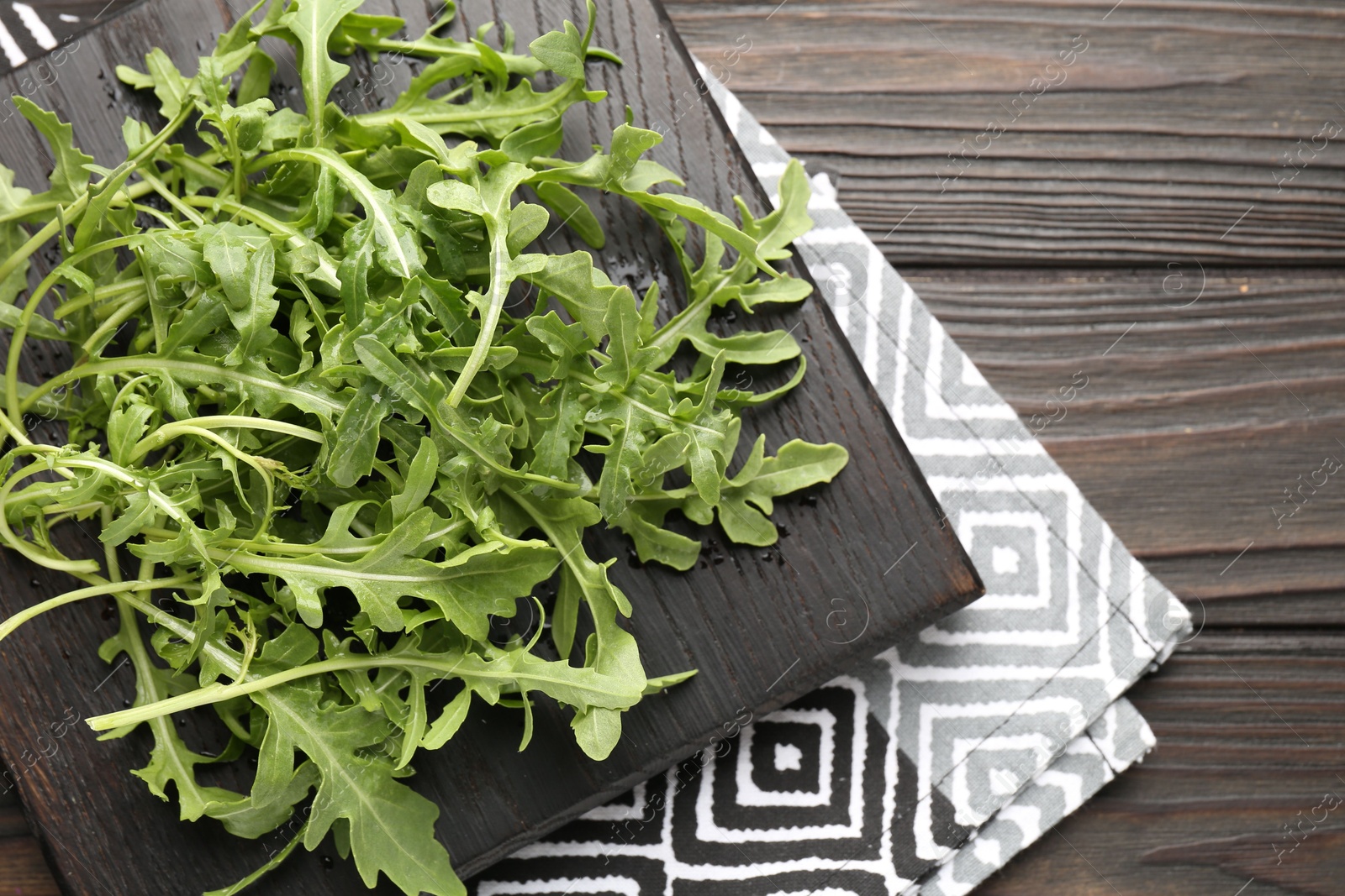 Photo of Fresh ripe green arugula leaves on dark wooden table, top view