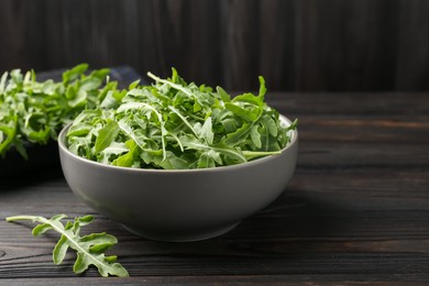 Photo of Fresh ripe green arugula leaves on dark wooden table, closeup. Space for text