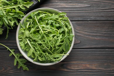 Photo of Fresh ripe green arugula leaves on dark wooden table, flat lay. Space for text