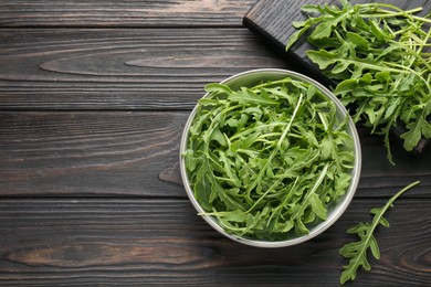 Photo of Fresh ripe green arugula leaves on dark wooden table, flat lay. Space for text