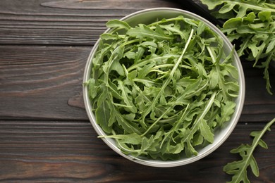 Photo of Fresh ripe green arugula leaves on dark wooden table, flat lay. Space for text