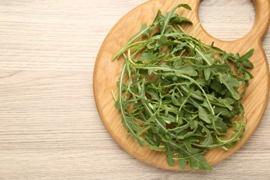Photo of Fresh ripe green arugula leaves on light wooden table, top view. Space for text