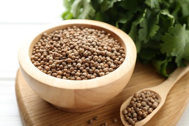 Photo of Coriander seeds and fresh cilantro on white wooden table, closeup