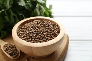 Photo of Coriander seeds and fresh cilantro on white wooden table, closeup