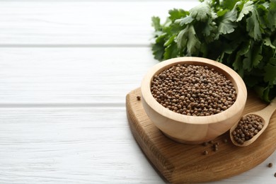 Photo of Coriander seeds and fresh cilantro on white wooden table, closeup. Space for text