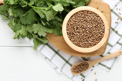 Photo of Coriander seeds and fresh cilantro on white wooden table, top view