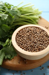 Photo of Coriander seeds and fresh cilantro on light blue wooden table, closeup