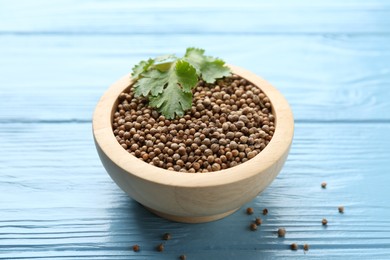Photo of Coriander seeds in bowl and fresh cilantro leaves on light blue wooden table, closeup
