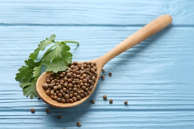 Photo of Coriander seeds, spoon and fresh cilantro leaves on light blue wooden table, closeup