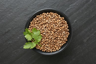 Photo of Coriander seeds and fresh cilantro leaves in bowl on dark textured table, top view