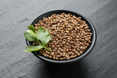 Photo of Coriander seeds and fresh cilantro leaves in bowl on dark textured table, closeup