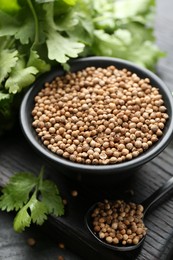 Photo of Coriander seeds in bowl, spoon and fresh cilantro leaves on dark table, closeup