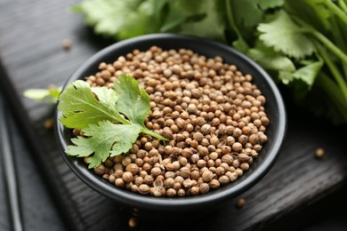 Photo of Coriander seeds and fresh cilantro leaves in bowl on dark table, closeup