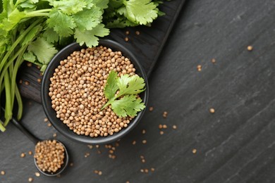 Photo of Coriander seeds in bowl, spoon and fresh cilantro leaves on dark textured table, flat lay. Space for text