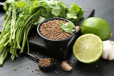 Photo of Coriander seeds in bowl, fresh cilantro, lime and garlic on dark textured table, closeup