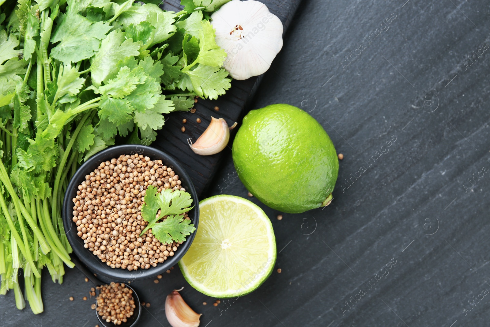Coriander seeds in bowl, fresh cilantro, lime and garlic on dark textured table, flat lay. Space for text Photo of Coriander seeds in bowl, fresh cilantro, lime and garlic on dark textured table, flat lay. Space for text