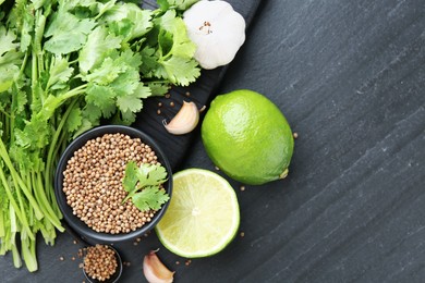 Photo of Coriander seeds in bowl, fresh cilantro, lime and garlic on dark textured table, flat lay. Space for text