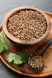 Photo of Coriander seeds in bowl, spoon and fresh cilantro leaves on dark textured table, closeup