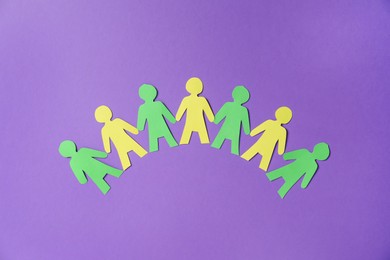 Photo of Paper figures of people holding hands on purple background, top view
