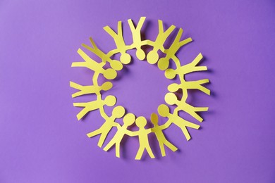 Photo of Paper figures of people holding hands on purple background, top view