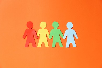 Photo of Paper figures of people holding hands on orange background, top view