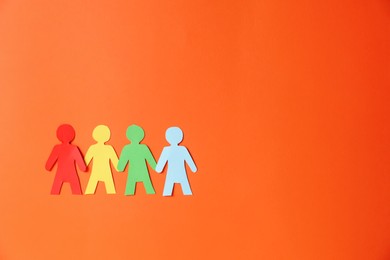 Photo of Paper figures of people holding hands on orange background, top view. Space for text