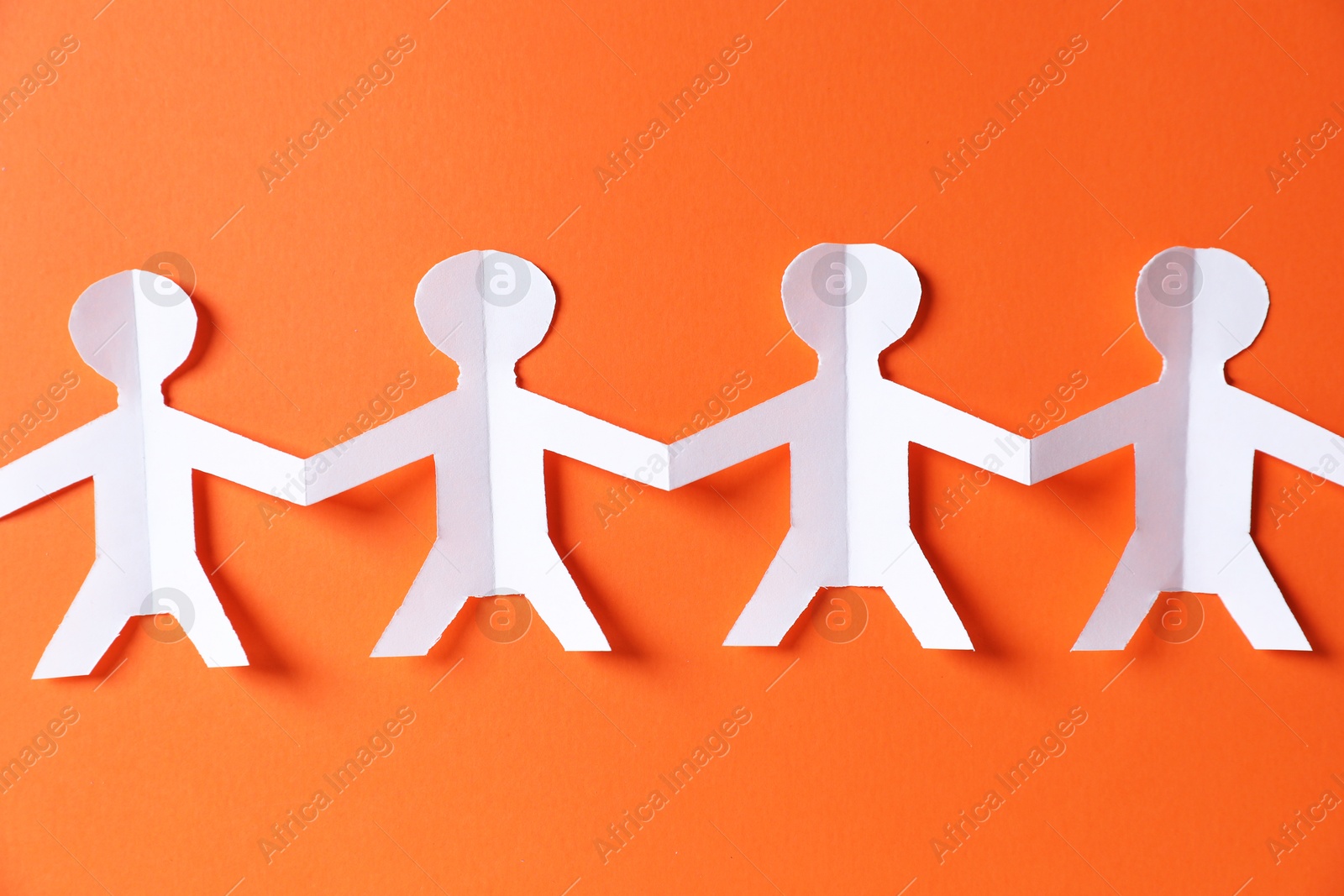 Paper figures of people holding hands on orange background, top view Photo of Paper figures of people holding hands on orange background, top view