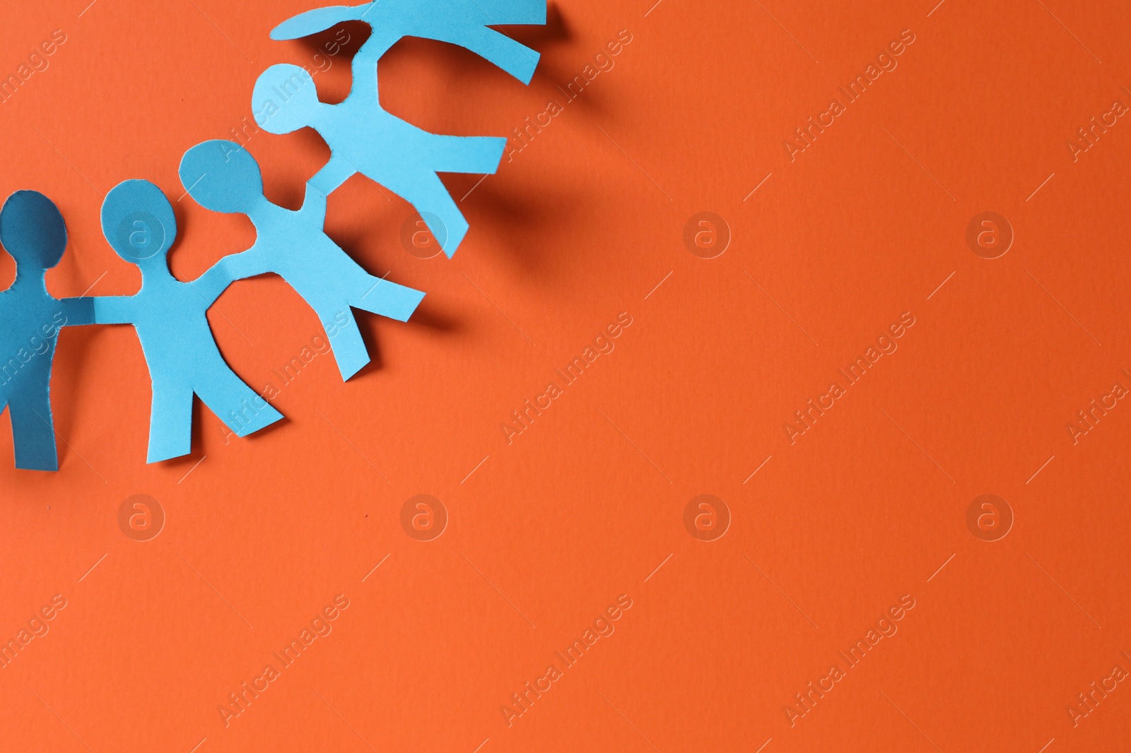 Paper figures of people holding hands on orange background, top view. Space for text Photo of Paper figures of people holding hands on orange background, top view. Space for text