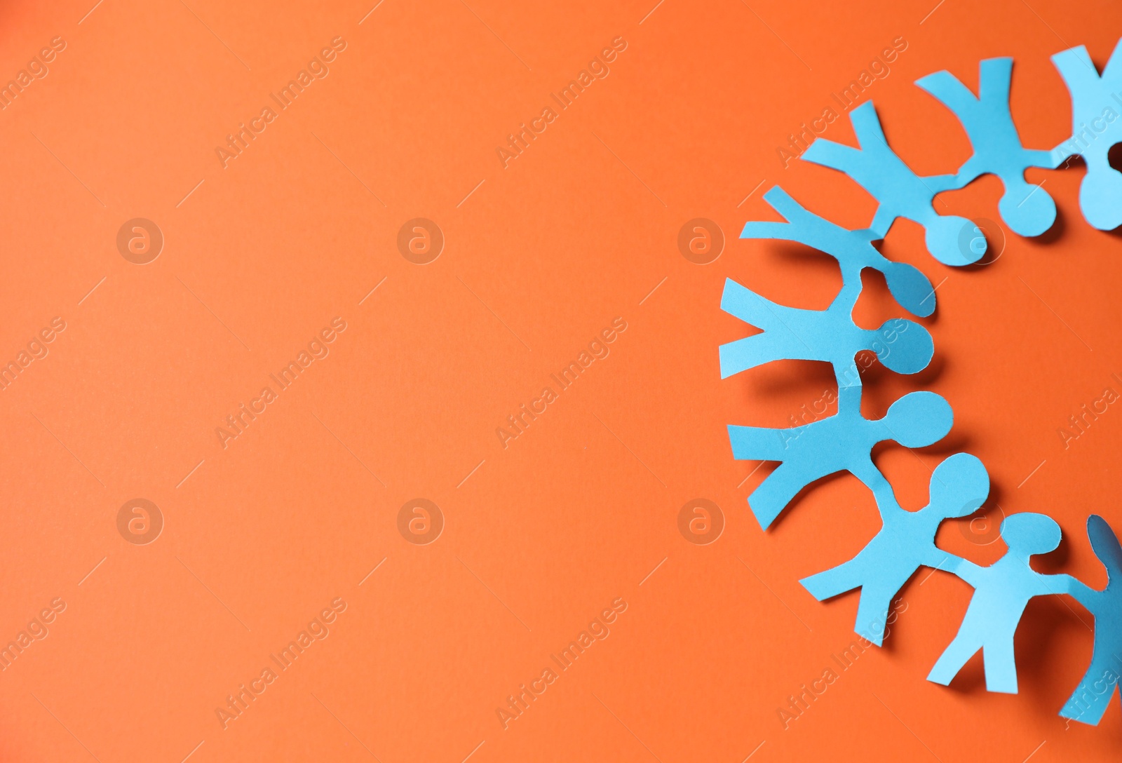 Photo of Paper figures of people holding hands on orange background, top view. Space for text