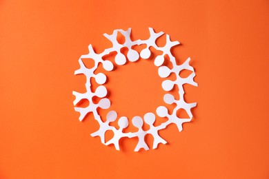 Photo of Paper figures of people holding hands on orange background, top view