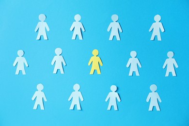 Photo of Paper human figures and yellow one on light blue background, flat lay