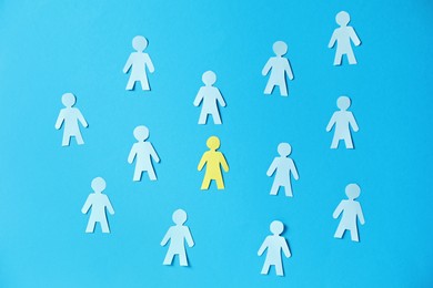 Photo of Paper human figures and yellow one on light blue background, flat lay