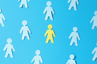 Photo of Paper human figures and yellow one on light blue background, flat lay
