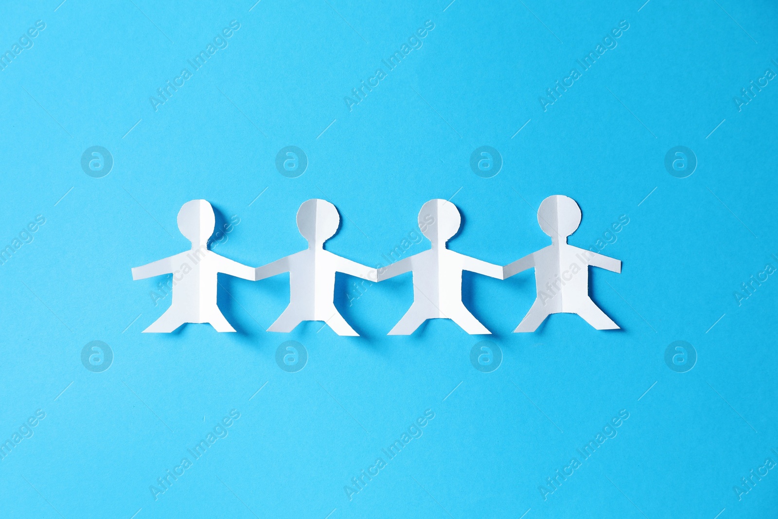 Paper figures of people holding hands on light blue background, top view Photo of Paper figures of people holding hands on light blue background, top view
