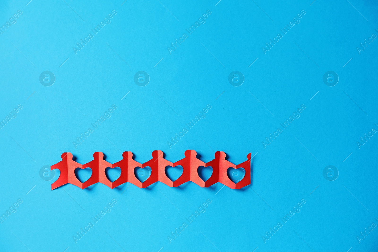 Paper figures of people holding hands on light blue background, top view. Space for text Photo of Paper figures of people holding hands on light blue background, top view. Space for text