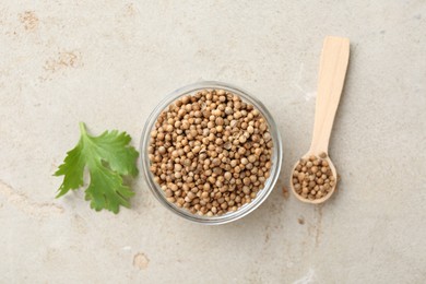 Photo of Coriander seeds in bowl, spoon and fresh cilantro leaf on color textured table, flat lay