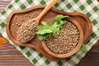 Photo of Coriander seeds in bowl, spoon and fresh cilantro sprigs on wooden table, top view
