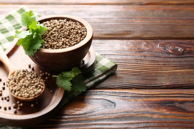 Photo of Coriander seeds and fresh cilantro sprigs on wooden table, closeup. Space for text