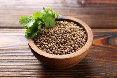 Photo of Coriander seeds and fresh cilantro leaves in bowl on wooden table, closeup