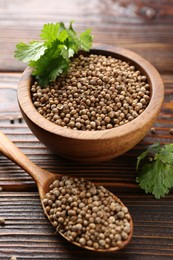 Photo of Coriander seeds and fresh cilantro leaves on wooden table, closeup