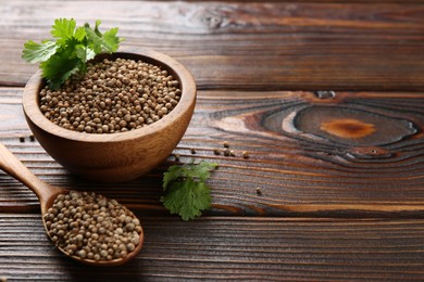 Photo of Coriander seeds and fresh cilantro sprigs on wooden table, closeup. Space for text