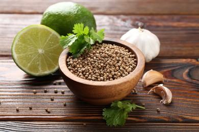 Photo of Coriander seeds, fresh cilantro, lime and garlic on wooden table, closeup