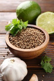 Photo of Coriander seeds, fresh cilantro, lime and garlic on wooden table, closeup