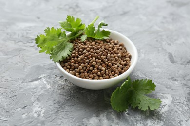 Photo of Coriander seeds in bowl and fresh cilantro sprigs on grey textured table, closeup