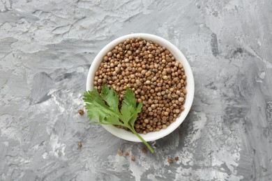 Photo of Coriander seeds and fresh cilantro sprig in bowl on grey textured table, top view