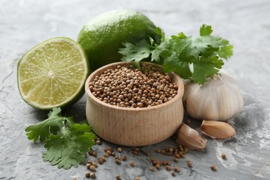 Photo of Coriander seeds, fresh cilantro, lime and garlic on grey textured table, closeup