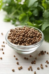 Photo of Coriander seeds in bowl and fresh cilantro leaves on light wooden table, closeup